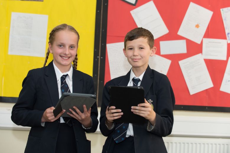 Two students with iPads in front of maths display